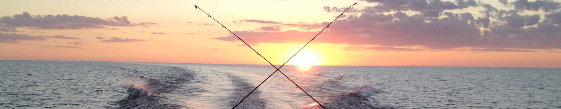 Sunset over the ocean with two fishing rods crossed in the foreground.