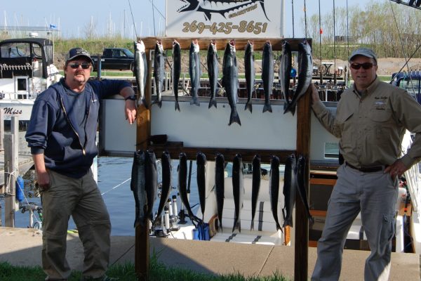 Two men proudly display a fresh catch of fish by the water.