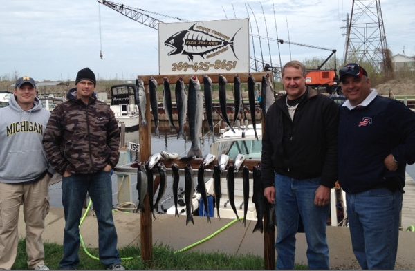 Two men posing with a large catch of fish displayed on a rack by the water.
